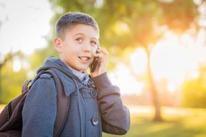 ung latinamerikan pojke gående utomhus med ryggsäck talande på cell telefon foto