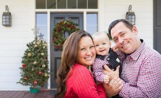 Lycklig ung familj på främre veranda av hus med jul dekorationer foto