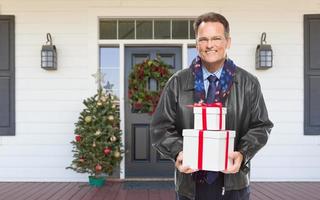 varmt klädd man innehav gåvor stående på jul dekorerad främre veranda foto