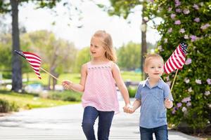 ung syster och bror vinka amerikan flaggor på de parkera foto