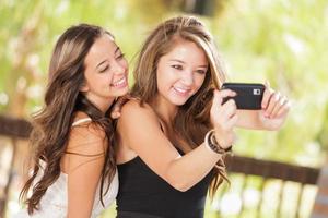 två attraktiv blandad lopp flick använder sig av deras smart cell telefoner för selfie utomhus foto