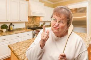 senior vuxen kvinna utskällning med de trä- sked inuti kök. foto