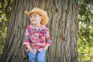 blandad lopp ung pojke bär cowboy hatt stående utomhus. foto