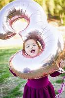 söt bebis flicka spelar med siffra tre mylar ballong utomhus foto