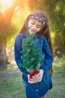 söt blandad lopp ung flicka innehav små jul träd utomhus foto