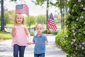 ung syster och bror vinka amerikan flaggor på de parkera foto