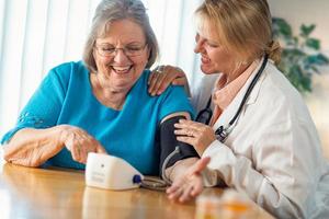 senior vuxen kvinna inlärning från kvinna läkare till använda sig av blod tryck maskin foto