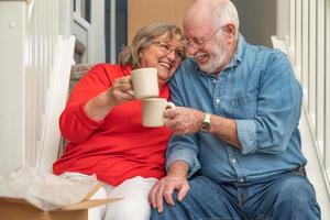 trött senior vuxen par vilar på trappa med koppar av kaffe omgiven med rör på sig lådor foto