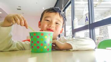 söt ung kinesisk och caucasian pojke njuter äter hans frysta yoghurt foto