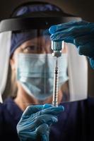 läkare eller sjuksköterska bär kirurgisk handskar innehav vaccin injektionsflaska och medicinsk spruta foto