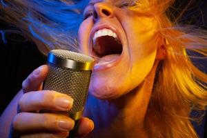 kvinna vokalist under gelade belysning sjunger med passionen in i kondensor mikrofon. foto
