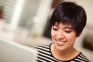 Söt leende multietnisk kvinna använder sig av bärbar dator foto