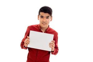 eleganta ung brunett man Framställ med tömma plakat i hans händer och leende på kamera isolerat på vit bakgrund foto