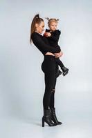 sexig ung mor i svart kläder håll henne liten dotter i händer foto