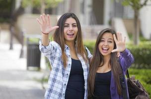 blandad lopp kvinna studenter vinka bärande ryggsäckar på skola campus foto