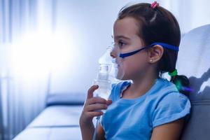 liten caucasian flicka är andas med särskild mask, som hjälper till sluta astma ge sig på eller lindra symptom av respiratorisk sjukdom. foto