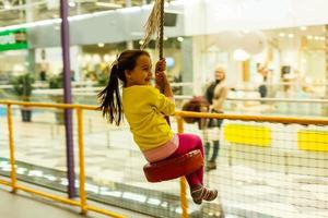 förtjusande liten flicka bungee gunga på de lekplats i gul. lycka, frihet, njutning, hälsa. foto