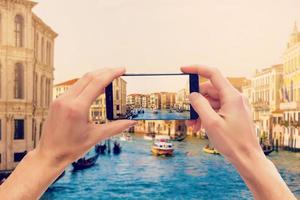 tar bilder på mobil smart telefon i gondol på kanal grande med klassisk gammal hus i de bakgrund, Venedig, Italien foto