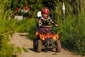 de liten flicka rider en quad cykel. en mini quad cykel är en Häftigt flicka i en hjälm och skyddande Kläder. elektrisk quad cykel elektrisk bil för barn populariserar grön teknologi foto