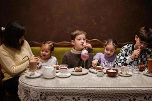 Lycklig familj äter desserter tillsammans på mysigt Kafé och har roligt. pojke unge dryck mjölk skaka. foto