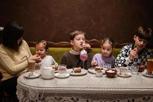 Lycklig familj äter desserter tillsammans på mysigt Kafé och har roligt. pojke unge dryck mjölk skaka. foto