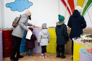 Lycklig liten barn med mor i en godis Lagra väljer sötsaker, marmelad godis, sätter dem i en papper väska. foto