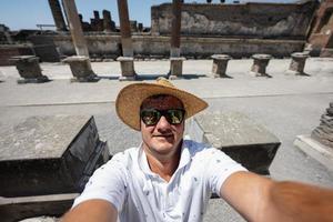 man turist i hatt och solglasögon framställning selfie på pompeii gammal stad, Italien. foto