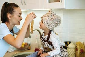 söt liten hemkock flicka med henne skön mor gör pannkakor i vit kök. foto