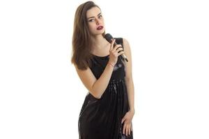 skön ung flicka i svart klänning innehav en mikrofon foto