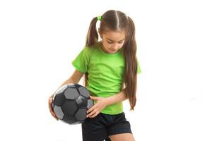 liten blond flicka i grön enhetlig spelar med fotboll boll foto