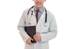 ung elegant läkare i enhetlig med stetoskop leende på kamera och göra anteckningar isolerat på vit bakgrund foto