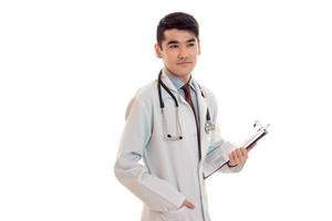 omtänksam Söt brunett manlig läkare i enhetlig med stetoskop på hans nacke Framställ i studio isolerat på vit bakgrund foto