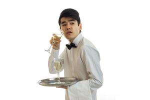 en ung servitör i en skjorta innehav glasögon med vit vin och utseende mot foto