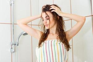 sexig ung flicka med våt hår står i de badrum i en handduk och stirrar ner foto