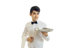 en ung servitör i chic skjorta utseende framåt- och händer i hand bricka foto