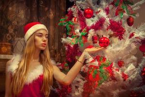 skön flicka i santa hatt nära jul träd foto