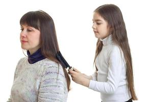 liten ung flicka gör en frisyr till henne mor foto