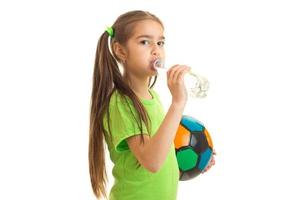 Söt liten flicka i grön enhetlig med fotboll boll drycker vatten foto