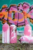 en få Begagnade måla burkar lögn på de jord nära de vägg med en skön graffiti målning i rosa och grön färger. gata konst begrepp foto