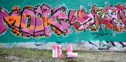 en få Begagnade måla burkar lögn på de jord nära de vägg med en skön graffiti målning i rosa och grön färger. gata konst begrepp foto
