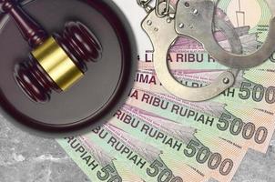 5000 indonesiska rupiah räkningar och bedöma hammare med polis handklovar på domstol skrivbord. begrepp av rättslig rättegång eller bestickning. beskatta undvikande foto