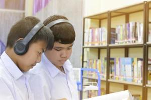 mjuk fucus av två asiatisk pojke studenter är lyssnande media, läsning och hört handla om favorit bok på bibliotek av skola foto