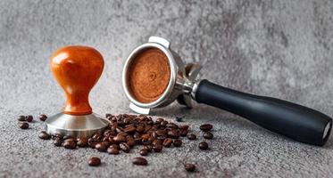 Utrustning i en kaffe affär av Barista kaffe verktyg portafilter med manipulera och mörk rostad kaffe bönor på grå bakgrund foto