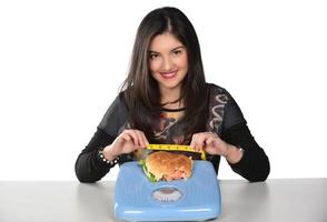 porträtt av en skön rolig ung flicka på de vit bakgrund, innehav en bricka burger med hamburgare och mätning skala foto