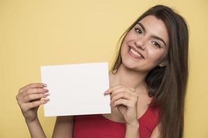 ung leende kvinna innehav en tom ark av papper för reklam foto