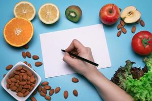 kreativ layout tillverkad av olika frukter, grönsaker och nötter med vit papper ark. platt lägga, blå bakgrund. fri Plats för text. friska mat begrepp. foto