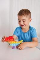 liten pojke spelar med regnbåge pop- den fidget leksak. antistress barn spel. barns trendig silikon leksaker pop- den till lindra påfrestning och utveckla hand motor Kompetens. färgrik hand leksak med skjuta på bubblor. foto