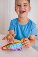 liten pojke spelar med regnbåge pop- den fidget leksak. antistress barn spel. barns trendig silikon leksaker pop- den till lindra påfrestning och utveckla hand motor Kompetens. färgrik hand leksak med skjuta på bubblor. foto