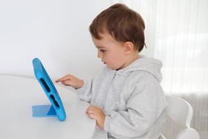 Lycklig liten pojke spelar spel på digital läsplatta på Hem. porträtt av en barn på Hem tittar på tecknad serie på de läsplatta. modern unge och utbildning teknologi. foto