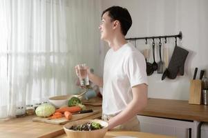 ett asiatisk ung man dricka färsk vatten i kök på Hem , friska livsstil begrepp foto